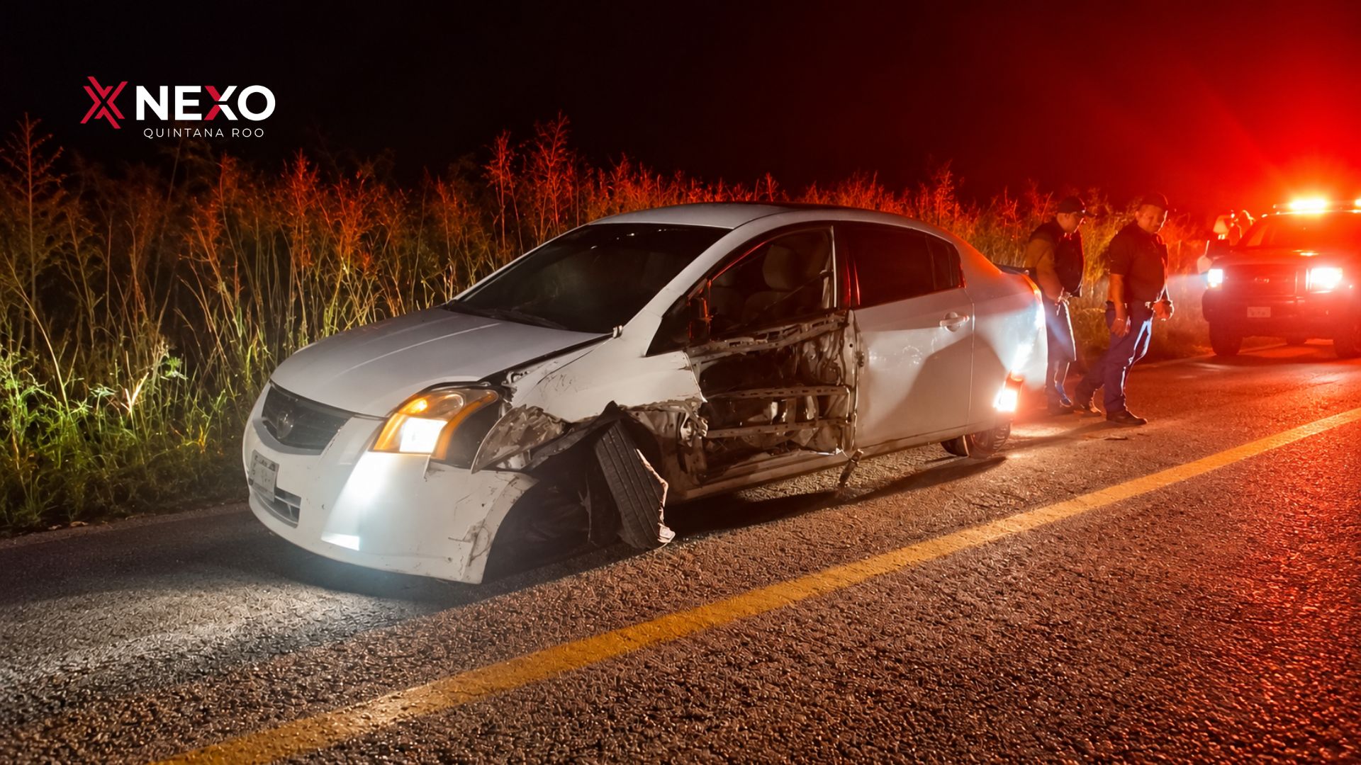 Un automóvil blanco presenta daños en la parte delantera y lateral izquierda tras un accidente carretero ocurrido durante la noche.