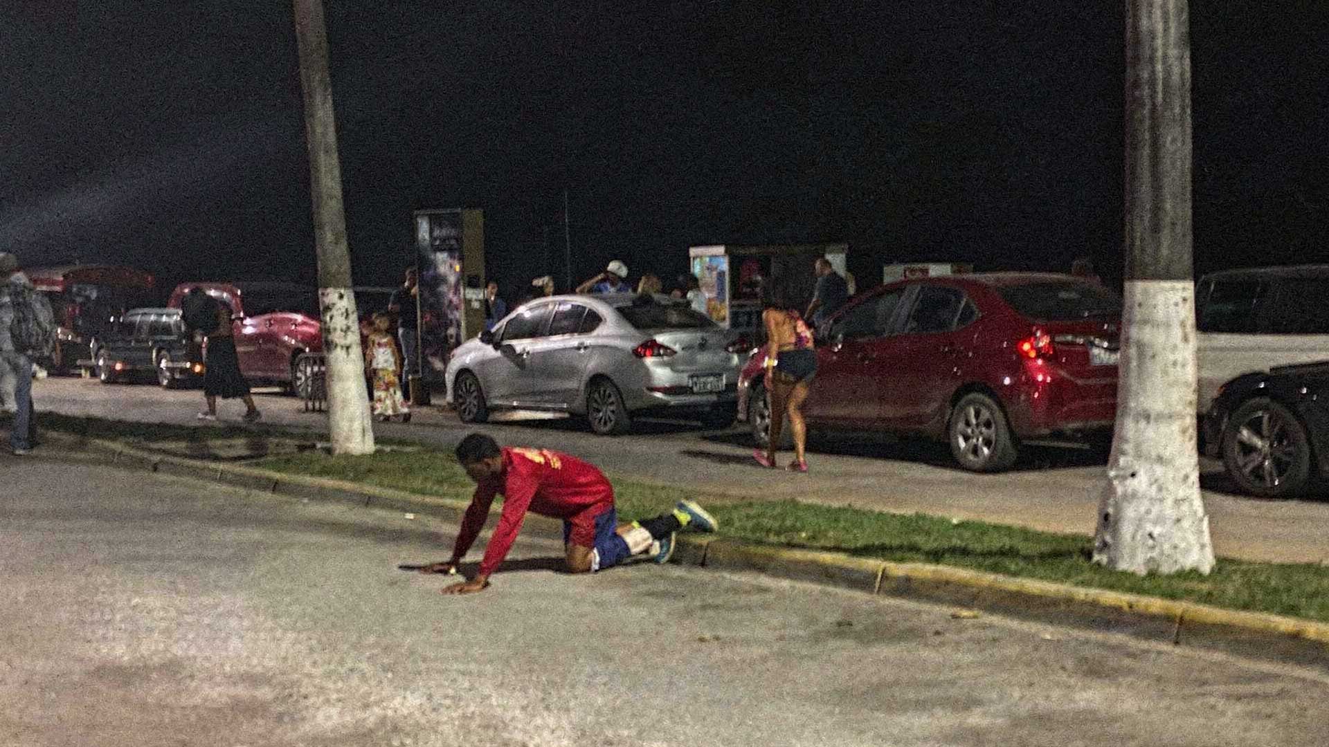 Varias personas reunidas junto a un automóvil durante la noche en el malecón de Cozumel