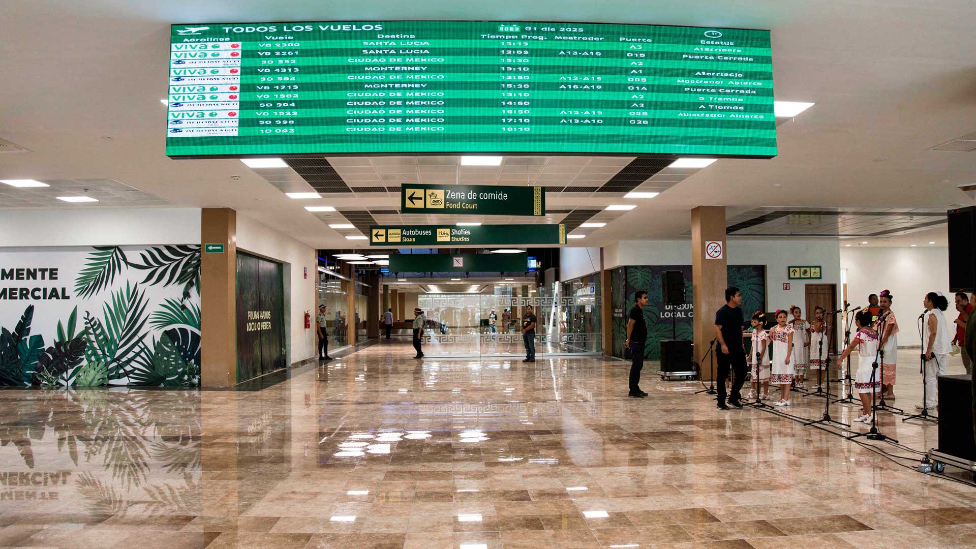 Interior de una terminal aeroportuaria con pasajeros, mostradores y señalización informativa de color verde